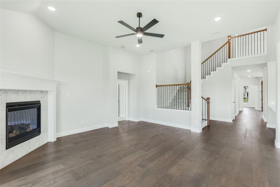 Open living room with dark hardwood floors, marble fireplace, ceiling fan, and staircase with iron balusters Open living room with dark hardwood floors, marble fireplace, ceiling fan, and staircase with iron balusters