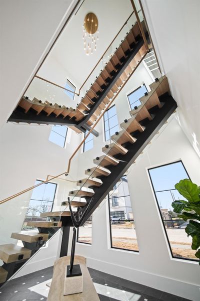 An incredible view of the modern floating staircase with glass panel railings from the first floor to the third floor.