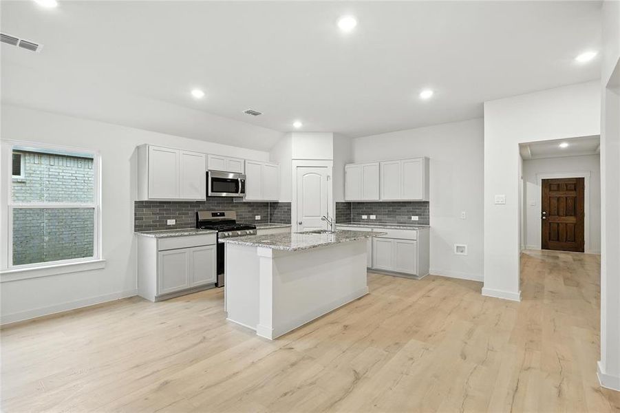 Kitchen featuring stainless steel appliances, decorative backsplash, light wood-type flooring, a center island with sink, and recessed lighting