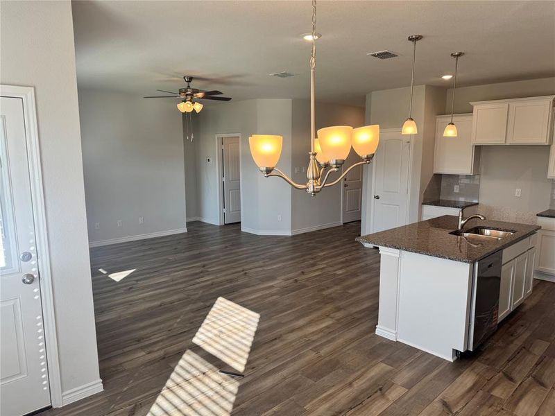 Kitchen featuring white cabinetry, decorative light fixtures, dark stone countertops, a kitchen island with sink, and a ceiling fan Kitchen featuring white cabinetry, decorative light fixtures, dark stone countertops, a kitchen island with sink, and a ceiling fan