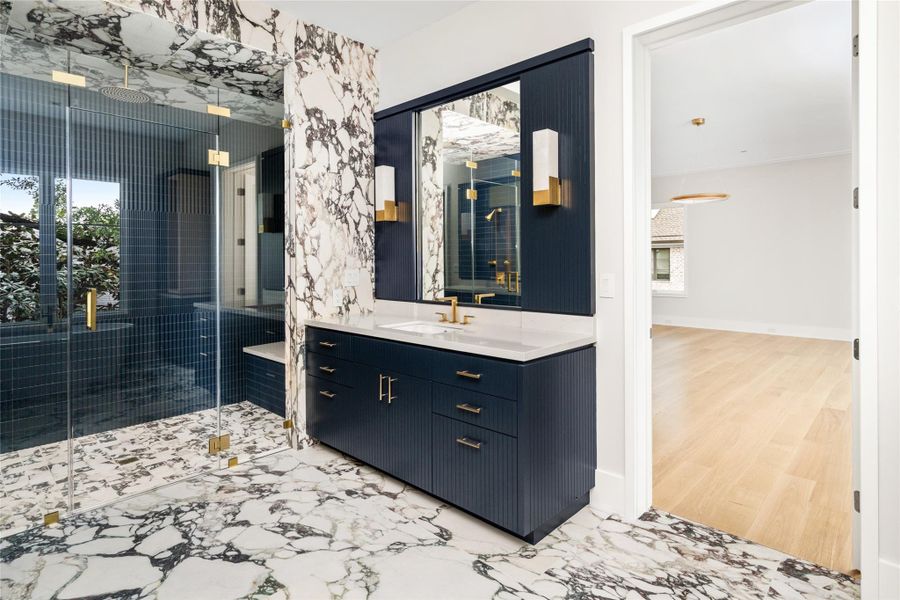 Dramatic surfaces wrap the space, complemented by fluted navy cabinetry and Kelly Wearstler sconces for a refined, layered finish.