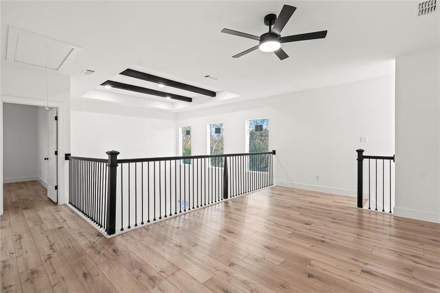 Unfurnished room featuring attic access, light wood-type flooring, a tray ceiling, and a ceiling fan