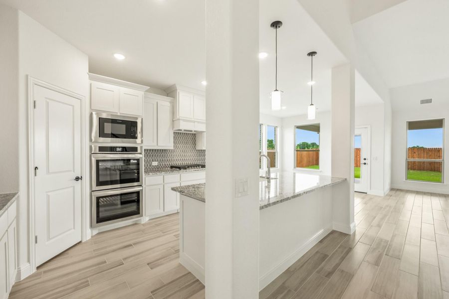 Open kitchen with white cabinets, granite island, stainless steel appliances, and pendant lights over light wood-look tile floors Open kitchen with white cabinets, granite island, stainless steel appliances, and pendant lights over light wood-look tile floors