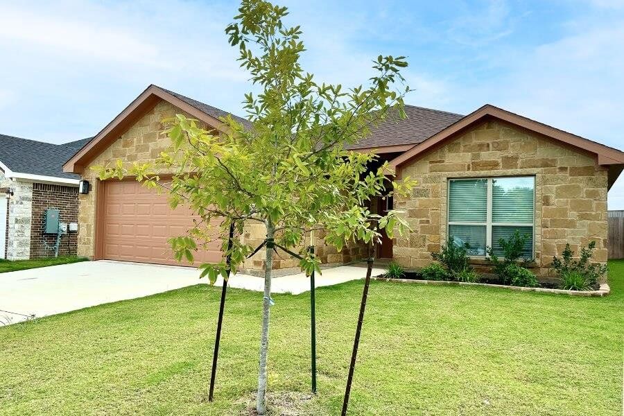 View of front of home with stone siding, concrete driveway, a front yard, and a shingled roof