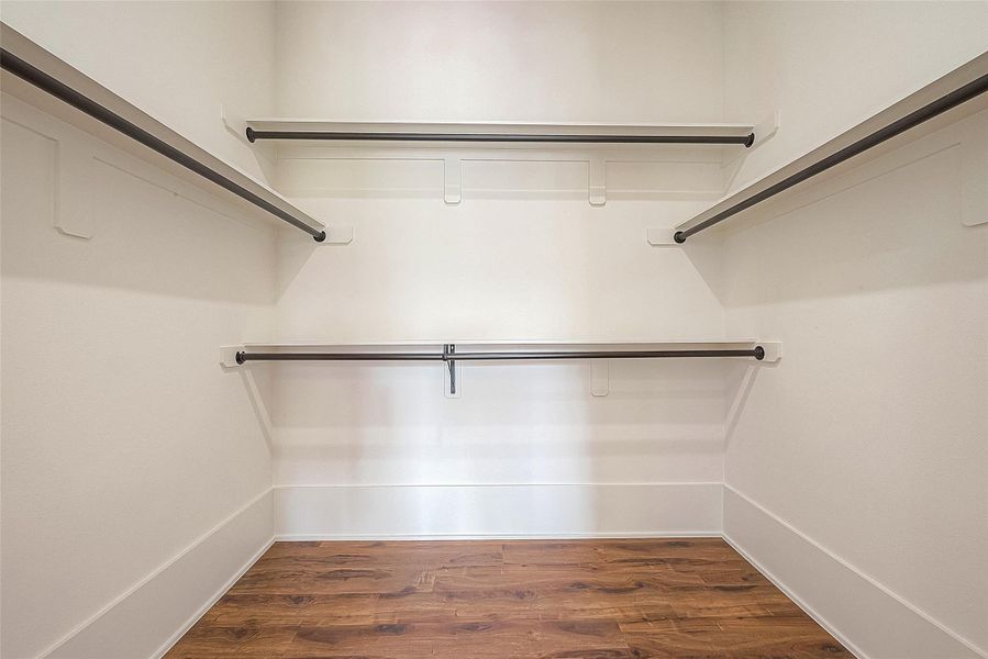 This is a clean, empty walk-in closet featuring multiple hanging rods for ample clothing storage and a hardwood floor for a modern touch. This is a clean, empty walk-in closet featuring multiple hanging rods for ample clothing storage and a hardwood floor for a modern touch.