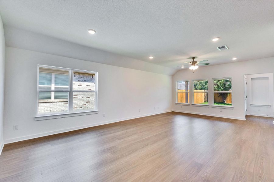 Open-concept living space with wood-finish flooring, vaulted ceiling, recessed lighting, and a ceiling fan