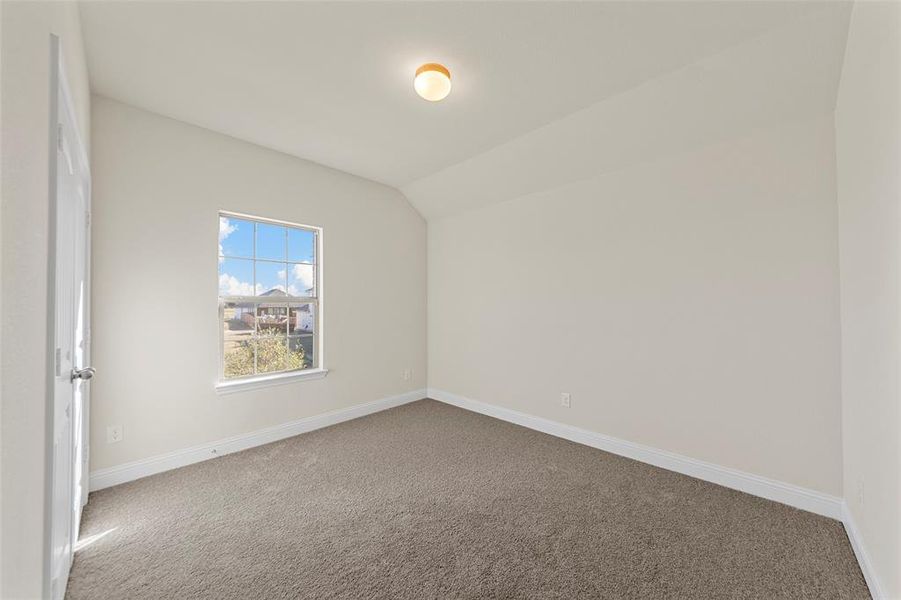 Carpeted spare room featuring vaulted ceiling