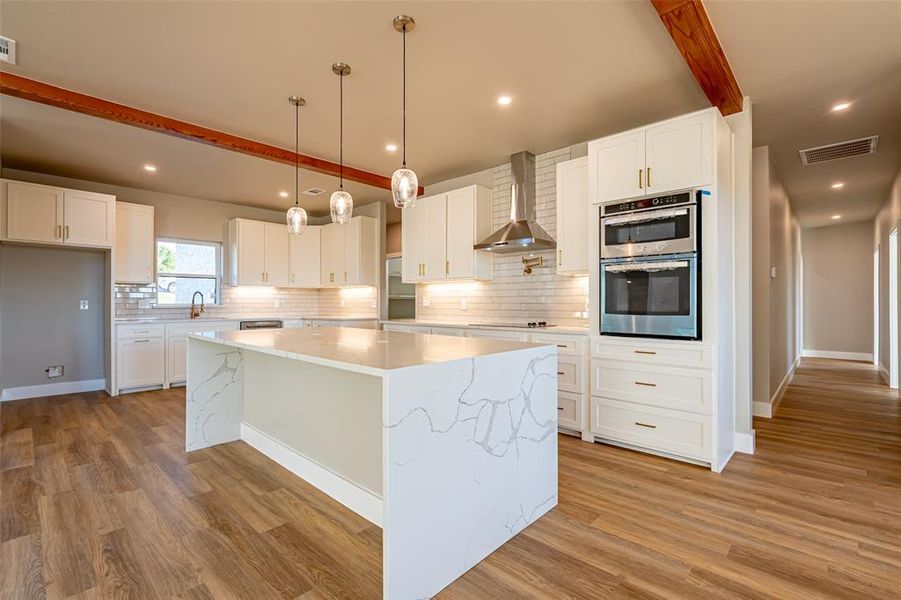Kitchen featuring beamed ceiling, a kitchen island, white cabinets, decorative backsplash, and light stone countertops Kitchen featuring beamed ceiling, a kitchen island, white cabinets, decorative backsplash, and light stone countertops