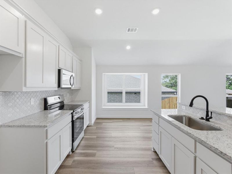 Contemporary kitchen featuring white cabinetry, light-toned countertops, a stainless steel sink with a matte black faucet, and wood-finish flooring Contemporary kitchen featuring white cabinetry, light-toned countertops, a stainless steel sink with a matte black faucet, and wood-finish flooring