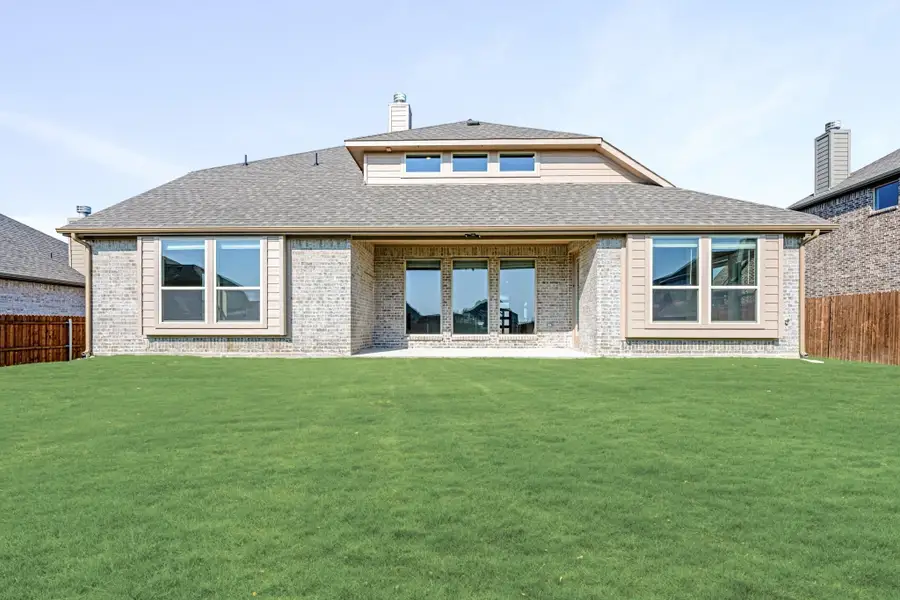 Rear exterior of brick home with large windows, covered patio entry, and spacious green backyard lawn