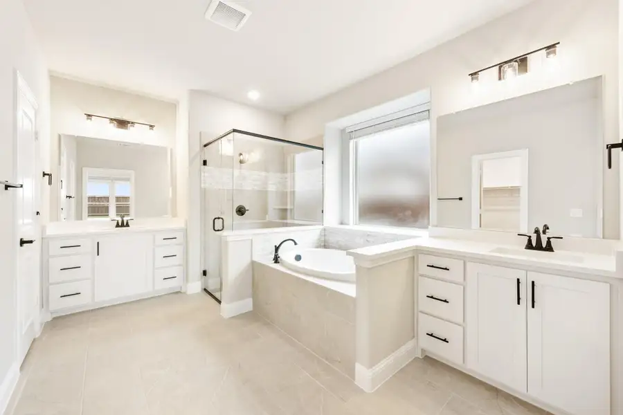 Master bathroom with dual vanities, corner soaking tub, and glass walk-in shower on tile floors