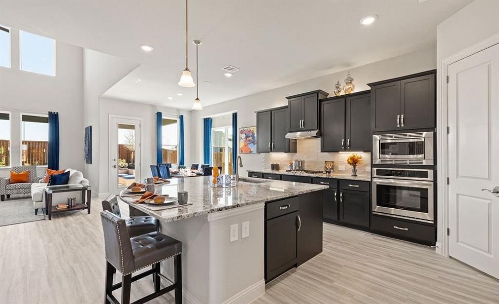 Kitchen featuring a kitchen island with sink, hanging light fixtures, sink, light stone countertops, and stainless steel appliances