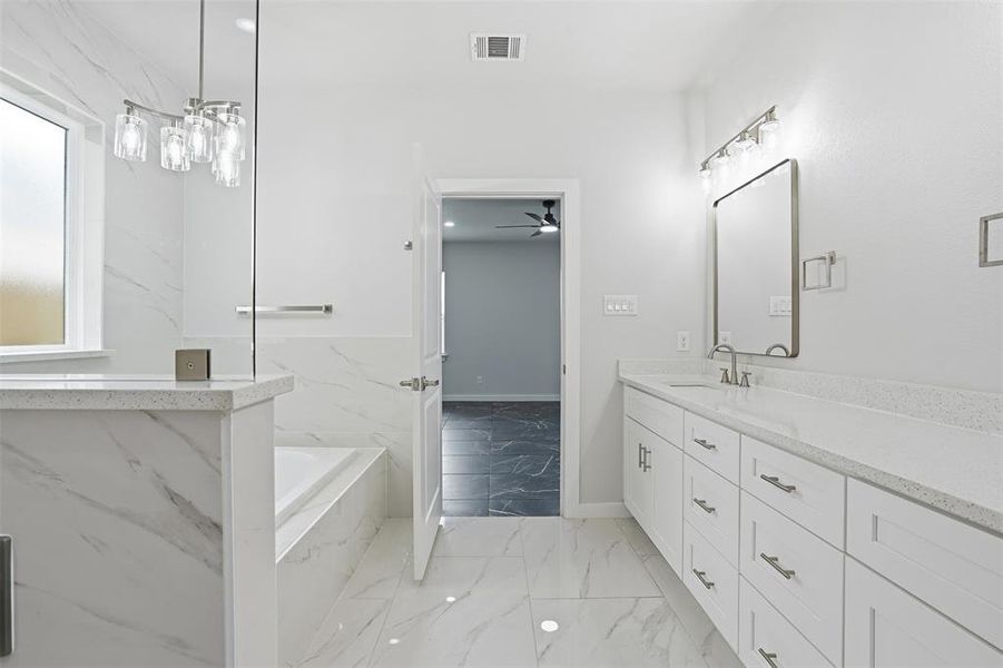 Spacious bathroom featuring white tiled flooring, a built-in soaking tub, a large vanity with dual sinks, and a separate glass-enclosed shower