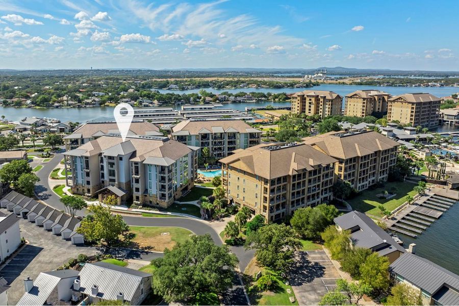 An aerial perspective reveals a serene lakeside community with residential buildings, a sparkling pool, and boat docks.