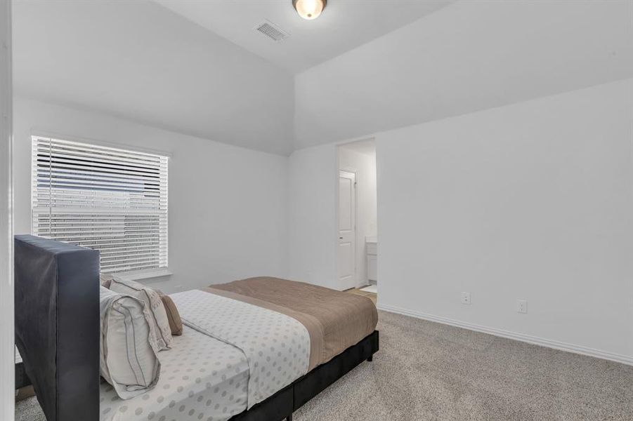 Bedroom with vaulted ceiling, connected bathroom, and light carpet