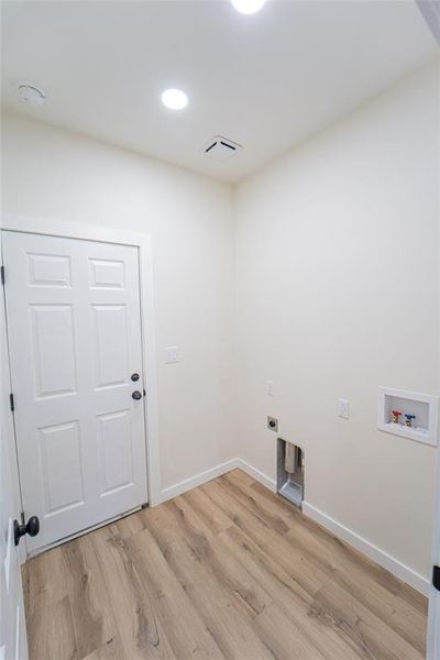 Utility room featuring wood-finish flooring, recessed lighting, and a white six-panel door with matte black hardware-located off of kitchen and within easy access to primary suite-