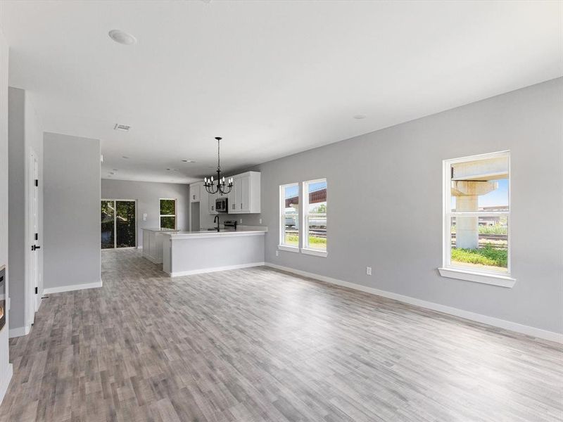 Unfurnished living room featuring light wood finished floors, a chandelier, baseboards, and a sink