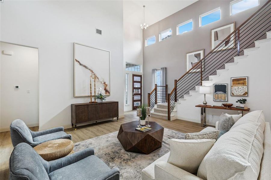 Two-story living area featuring wood-finish flooring, a contemporary staircase with horizontal metal balusters, and a tiered window arrangement