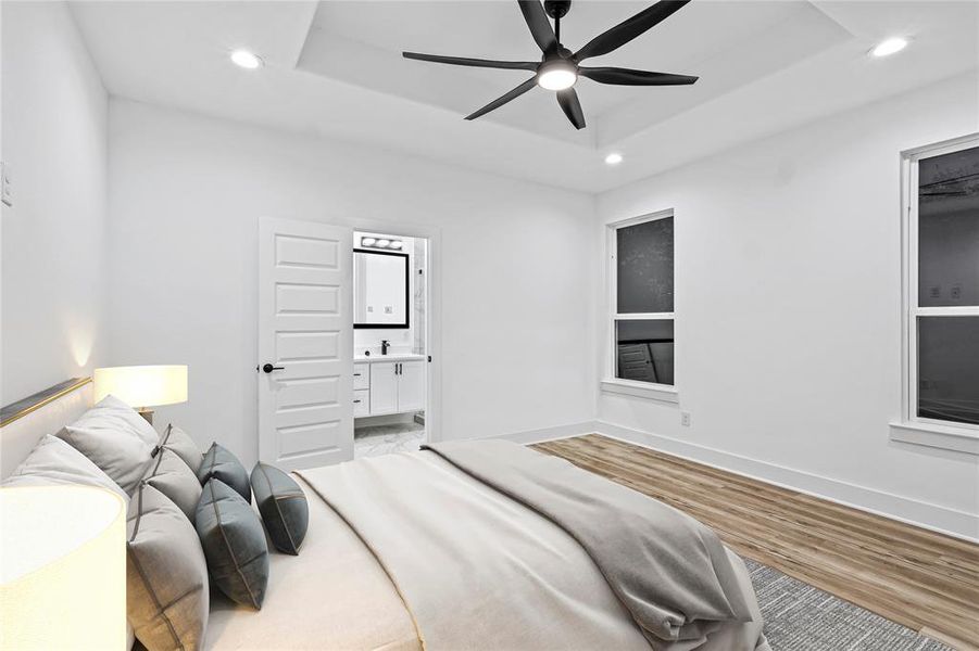 Bedroom with a raised ceiling, sink, light hardwood / wood-style flooring, ensuite bath, and ceiling fan