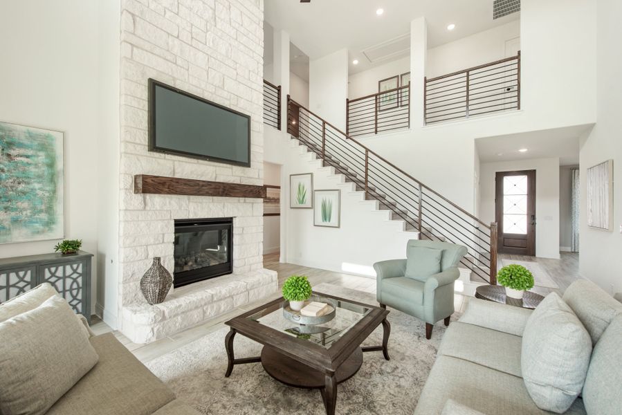 Open living room with two-story ceiling, white stone fireplace, wall-mounted TV, and staircase with metal railing Open living room with two-story ceiling, white stone fireplace, wall-mounted TV, and staircase with metal railing