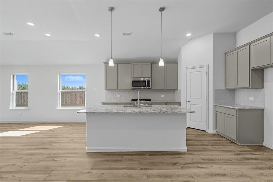 Kitchen with gray cabinetry, light stone countertops, stainless steel microwave, hanging light fixtures, and recessed lighting Kitchen with gray cabinetry, light stone countertops, stainless steel microwave, hanging light fixtures, and recessed lighting