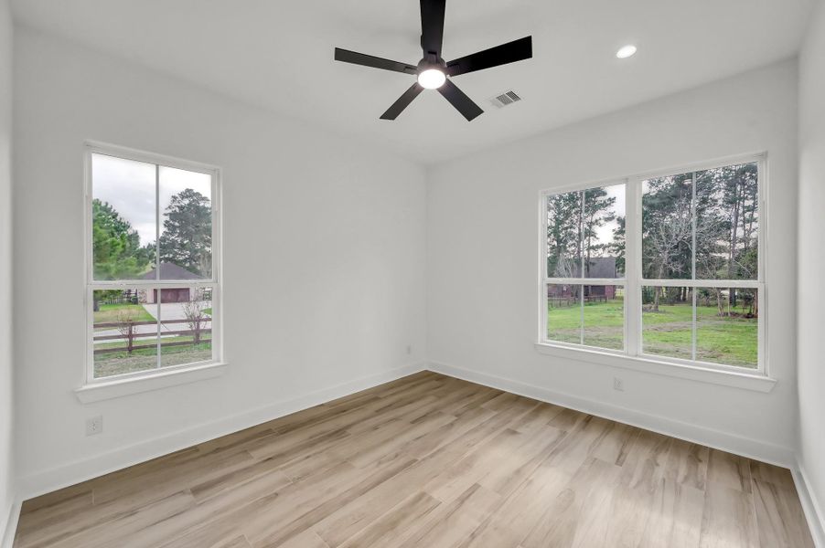 Bright secondary bedroom featuring large windows, modern ceiling fan, and wood-look flooring that continues throughout the home.