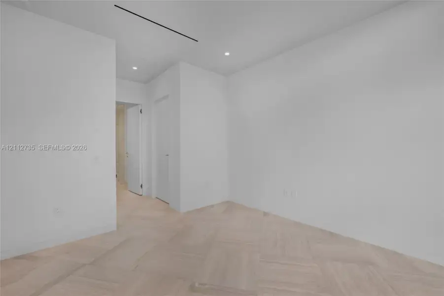 Minimalist interior featuring wood-finish parquet flooring, recessed ceiling lighting, and linear recessed ceiling detailing