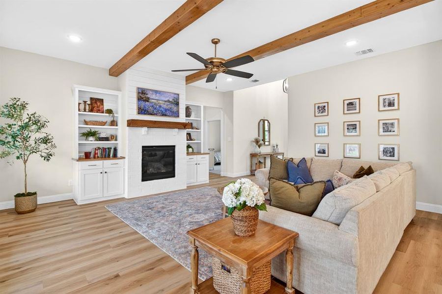 Living area with ceiling fan, beamed ceiling, a large fireplace, light wood-style floors, and recessed lighting Living area with ceiling fan, beamed ceiling, a large fireplace, light wood-style floors, and recessed lighting
