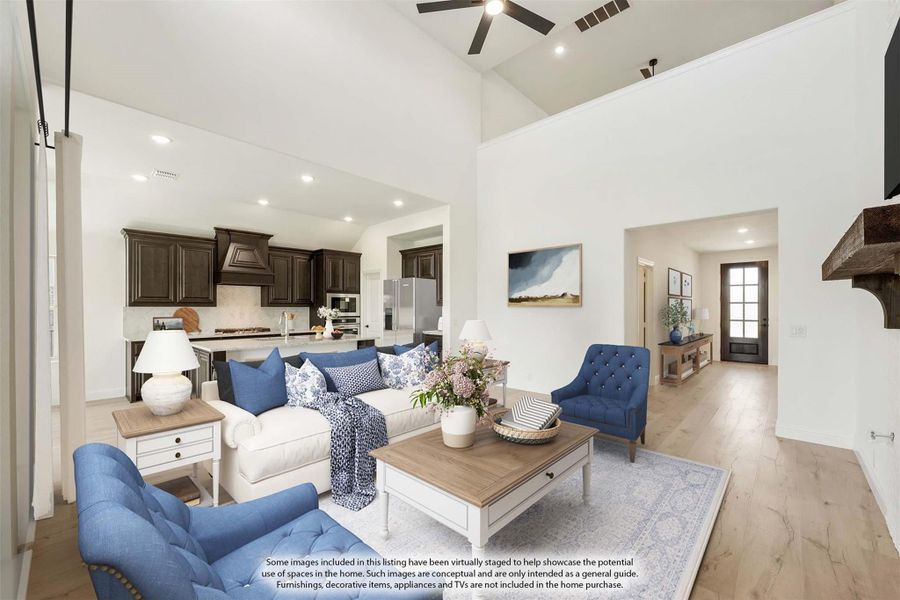 Open-concept living room with vaulted ceiling, blue seating, and dark wood kitchen cabinets visible in background