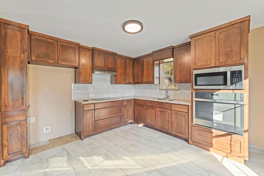 Kitchen featuring decorative backsplash, brown cabinets, appliances with stainless steel finishes, and light stone counters Kitchen featuring decorative backsplash, brown cabinets, appliances with stainless steel finishes, and light stone counters