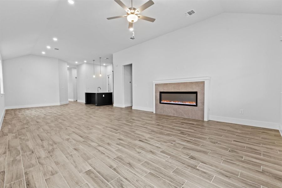 Unfurnished living room featuring ceiling fan, vaulted ceiling, and a tile fireplace