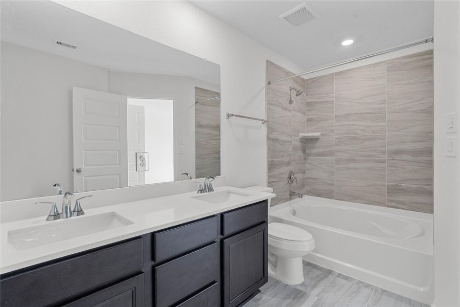 The primary bathroom offers a spacious tub/shower combination with a tiled surround, stained cabinetry topped with light countertops, dual sinks, high ceilings, neutral paint, a large mirror, and sleek, modern finishes for a polished look. The primary bathroom offers a spacious tub/shower combination with a tiled surround, stained cabinetry topped with light countertops, dual sinks, high ceilings, neutral paint, a large mirror, and sleek, modern finishes for a polished look.