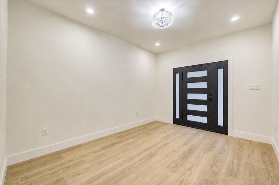 Elegant entryway featuring a modern black door with frosted glass panels, complemented by sleek LVP flooring and recessed lighting.