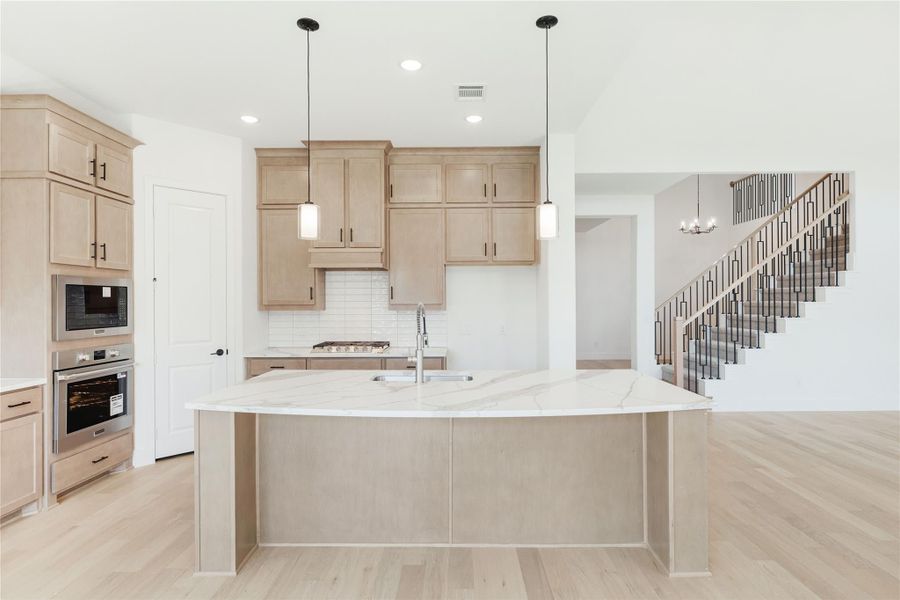 Kitchen with large marble island, light wood cabinets, stainless steel appliances, and pendant lights over hardwood floors