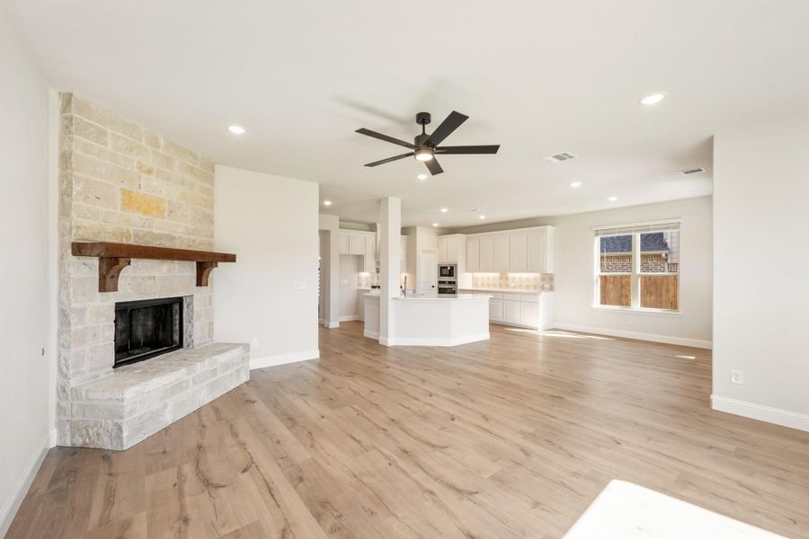 Open living area with stone fireplace, wood mantel, hardwood floors, and open kitchen with white cabinets in background
