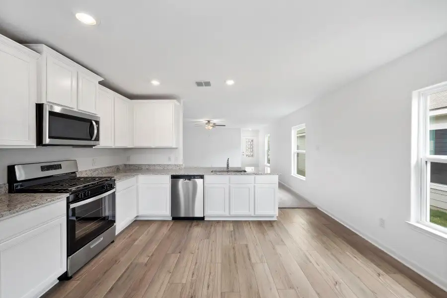 A pristine kitchen features sleek stainless steel appliances, granite countertops, and durable plank flooring.
