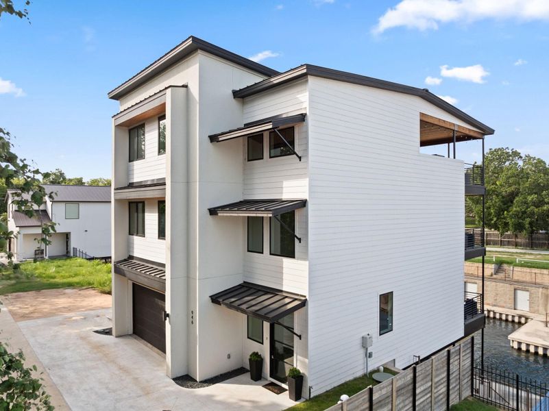 Modern three-story home with a sleek design, featuring large windows and 3 covered balconies. It has a two-car garage and is situated on a canal, offering attractive water views. The exterior is finished with clean white siding and dark trim accents.  This home is approved for short term rentals as well!