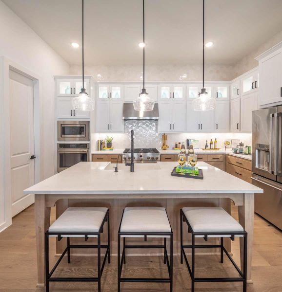 Kitchen with stainless steel appliances, light countertops, white cabinetry, wall chimney range hood, and tasteful backsplash