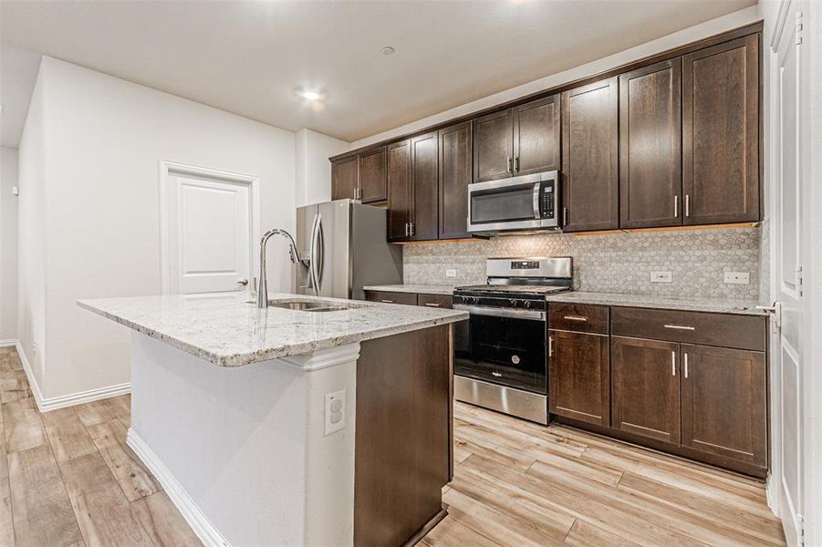 Kitchen featuring a center island with sink, light wood-style floors, tasteful backsplash, and appliances with stainless steel finishes