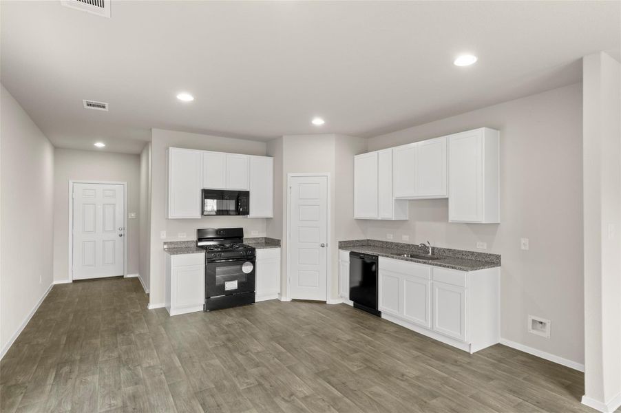 Kitchen with black appliances, recessed lighting, wood finished floors, white cabinetry, and dark stone countertops