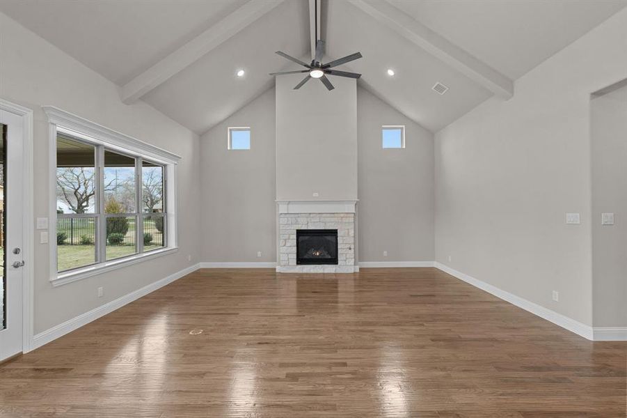 Unfurnished living room featuring beamed ceiling, hardwood / wood-style flooring, ceiling fan, and a stone fireplace. Not actual home. Previous built example.