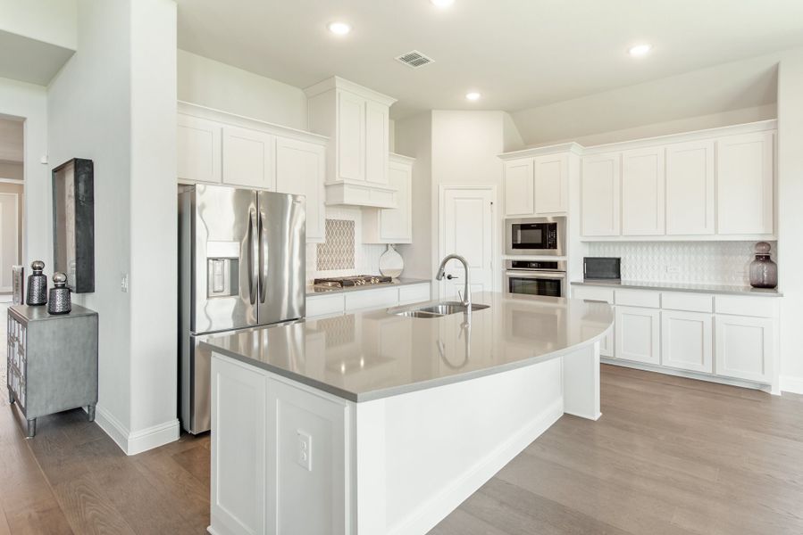 Kitchen with white cabinets, large center island with sink, stainless steel appliances, and hardwood floors Kitchen with white cabinets, large center island with sink, stainless steel appliances, and hardwood floors