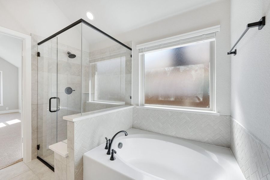 Master bathroom with soaking tub, herringbone tile surround, and glass-enclosed walk-in shower with black fixtures