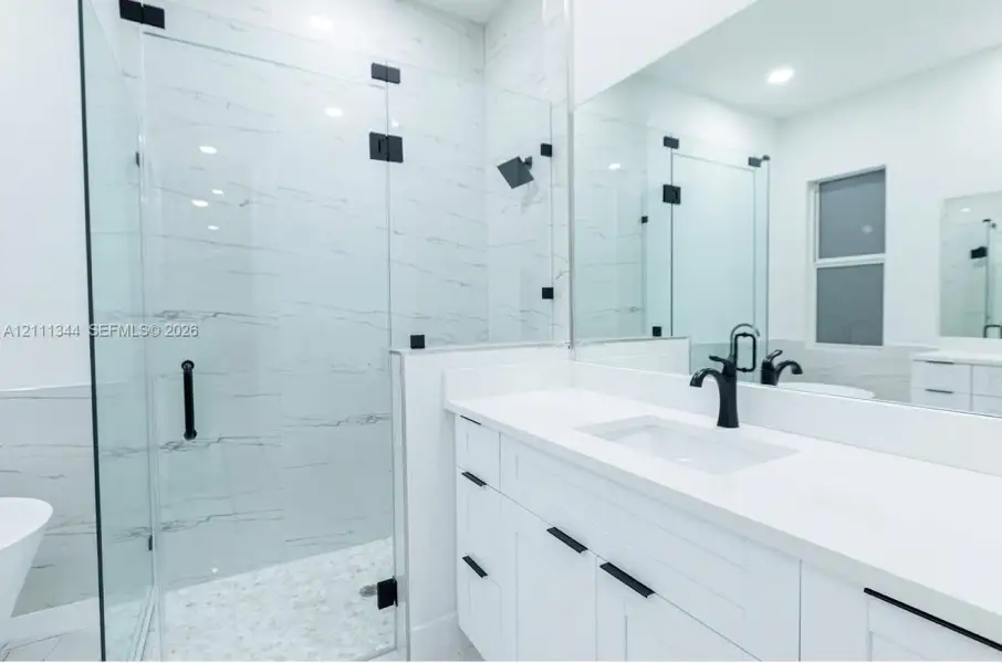 Walk-in shower with floor-to-ceiling tile, frameless glass enclosure, and matte black fixtures, paired with a white vanity featuring a stone-surface countertop and matte black hardware Walk-in shower with floor-to-ceiling tile, frameless glass enclosure, and matte black fixtures, paired with a white vanity featuring a stone-surface countertop and matte black hardware