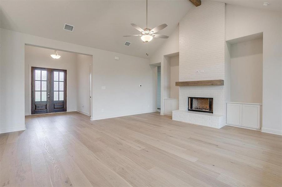 Unfurnished living room featuring french doors, a fireplace, high vaulted ceiling, ceiling fan, and light wood-type flooring