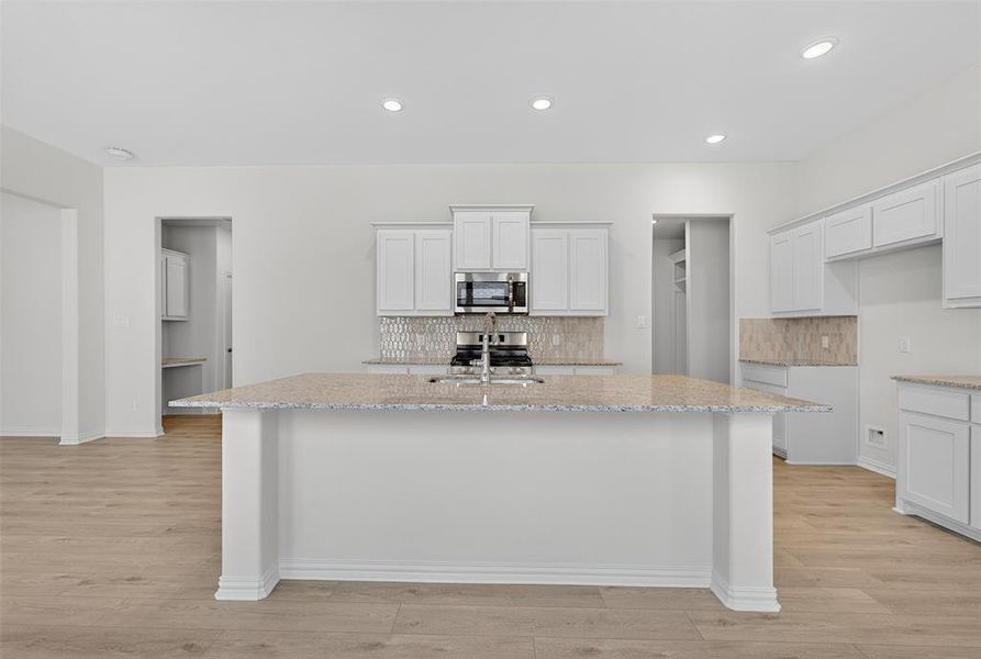 Kitchen with light stone counters, white cabinetry, backsplash, and recessed lighting