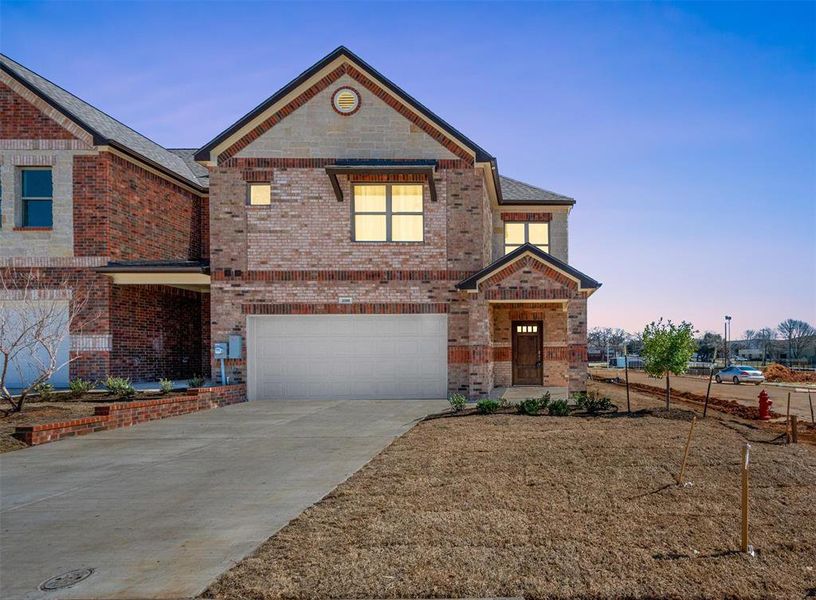 View of front facade with brick siding, driveway, and an attached garage