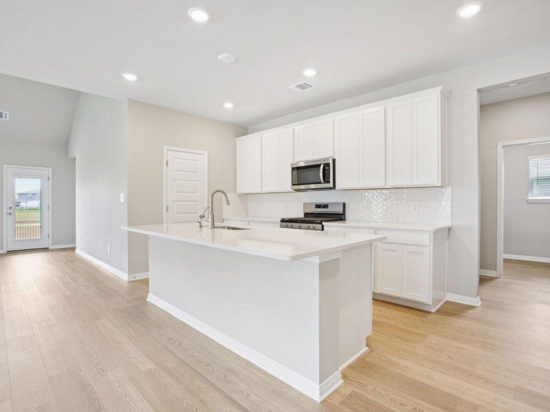 Kitchen featuring appliances with stainless steel finishes, a sink, a kitchen island with sink, light wood-style flooring, and backsplash Kitchen featuring appliances with stainless steel finishes, a sink, a kitchen island with sink, light wood-style flooring, and backsplash