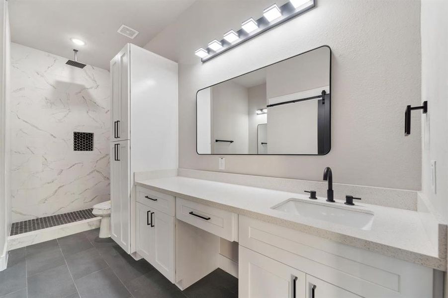 Shown here is one of two sinks, a convenient vanity area, and a linen closet, along with a spacious walk-in shower featuring a relaxing rain showerhead.