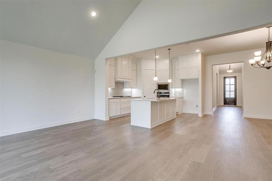 Kitchen with a center island with sink, pendant lighting, high vaulted ceiling, and light hardwood / wood-style floors